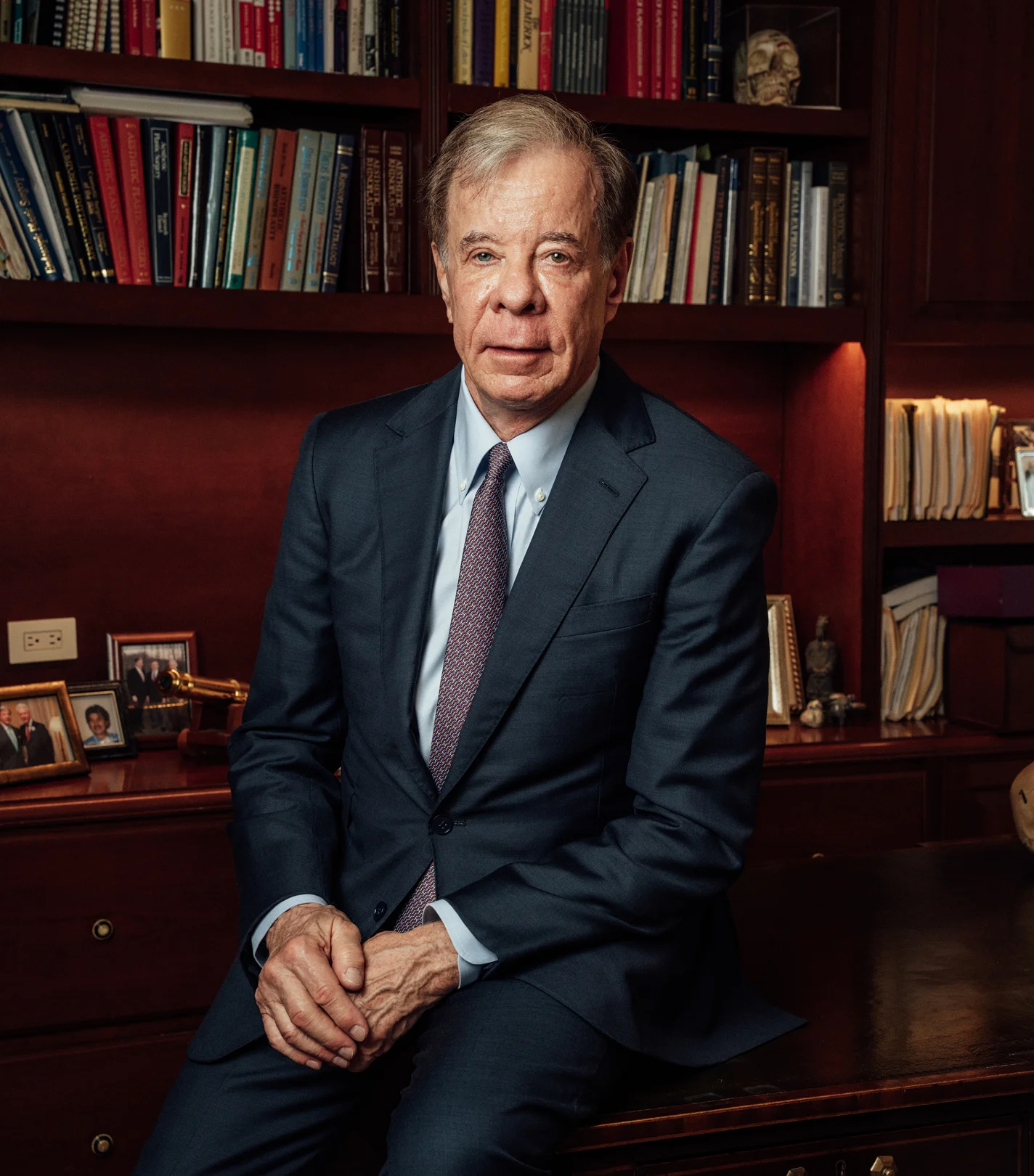 Dr Antell in navy suit sitting at desk in library office with bookshelves - in New York, NY
