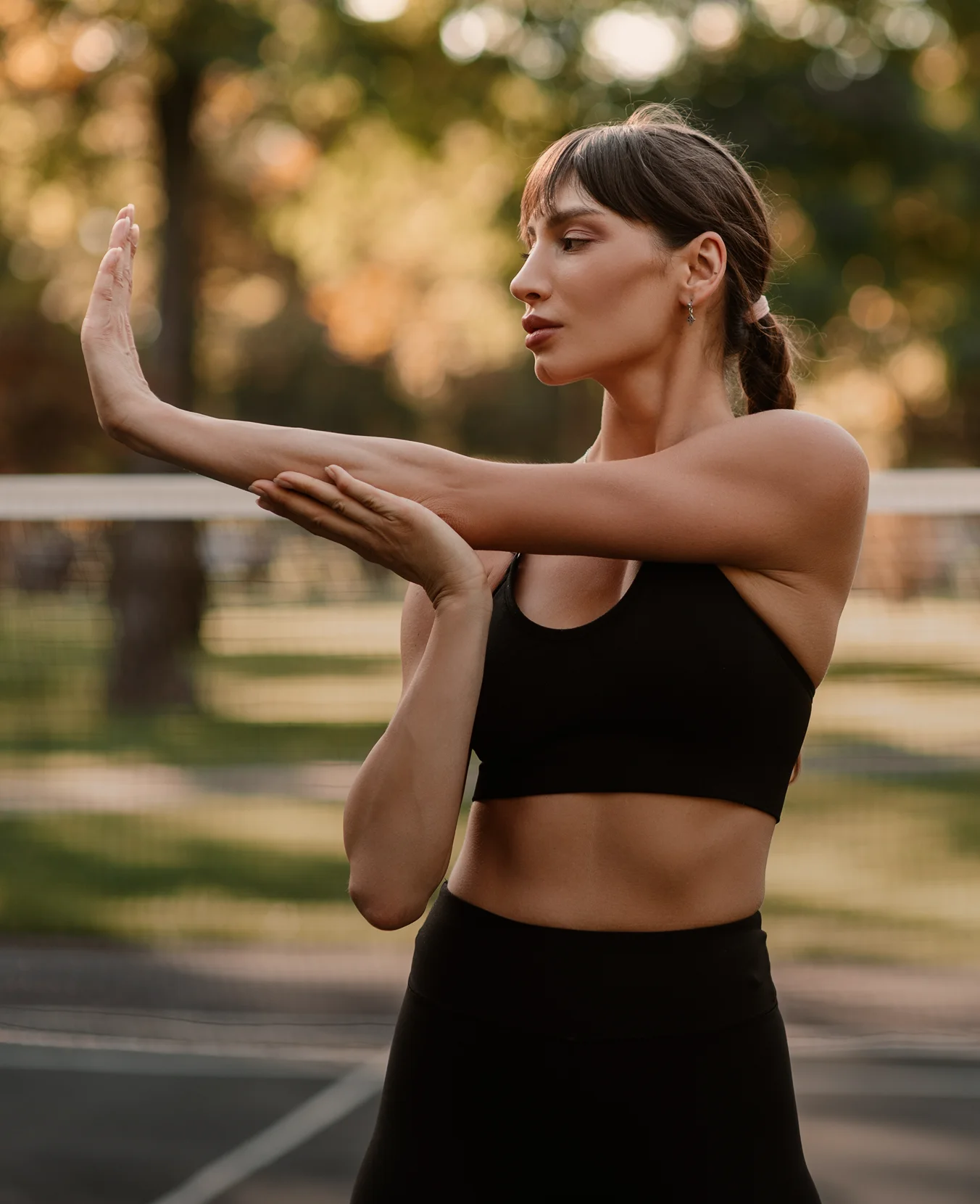 Woman in black athletic wear stretching her arm outdoors during fitness workout in park - body in New York, NY