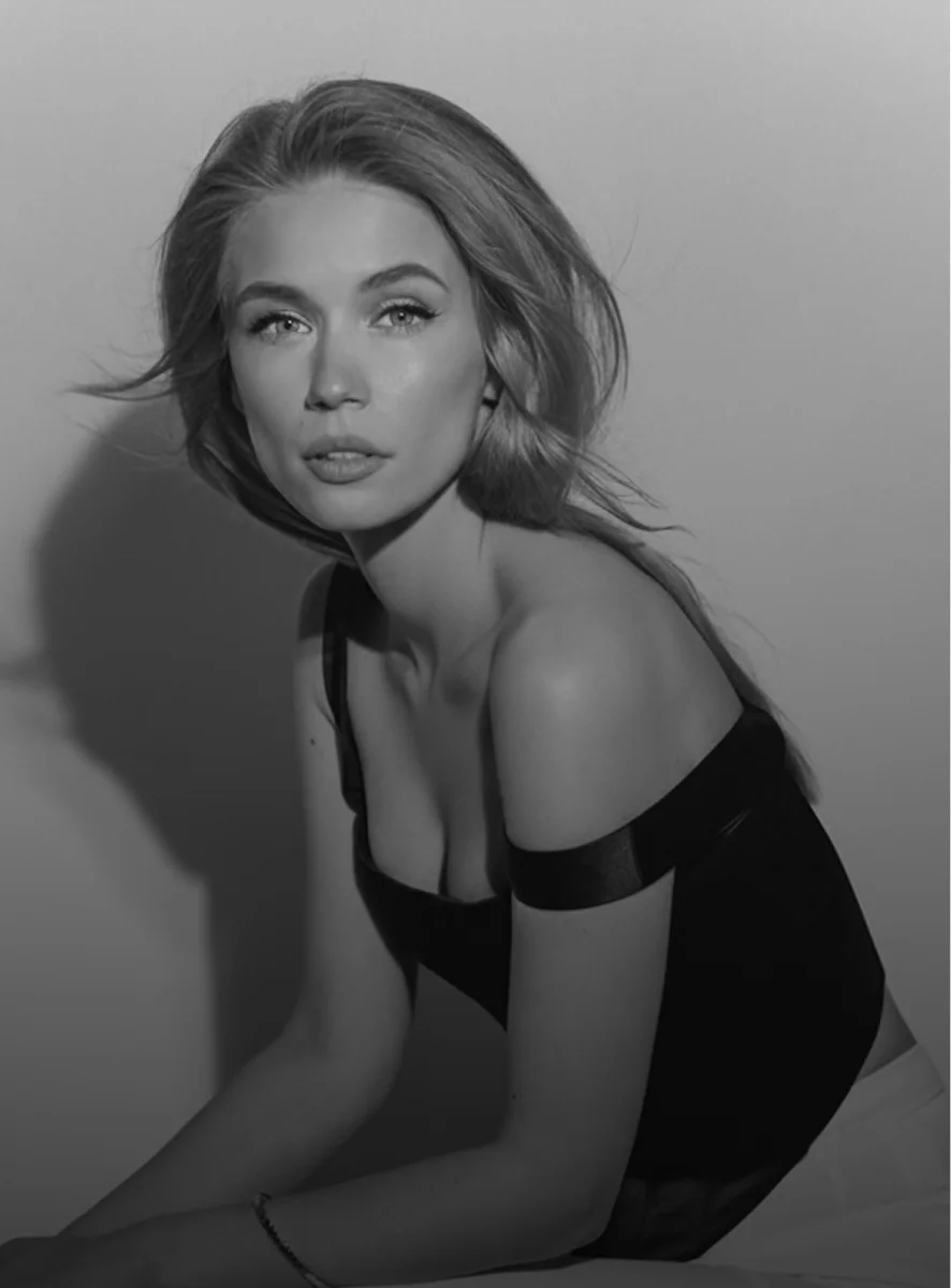 Elegant woman in black off-shoulder dress posing against white wall in black and white portrait photography - breast in New York, NY