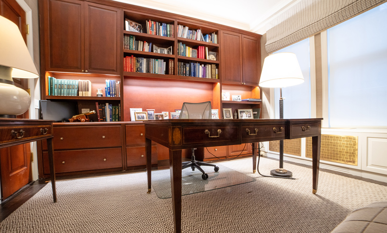 Professional home office with wood furniture, built-in bookshelves, dual desks, and natural lighting