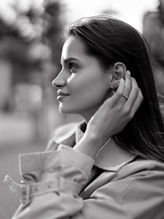 Young woman in profile view touching hair while holding coffee cup outdoors in black and white - about chin implants in New York, NY
