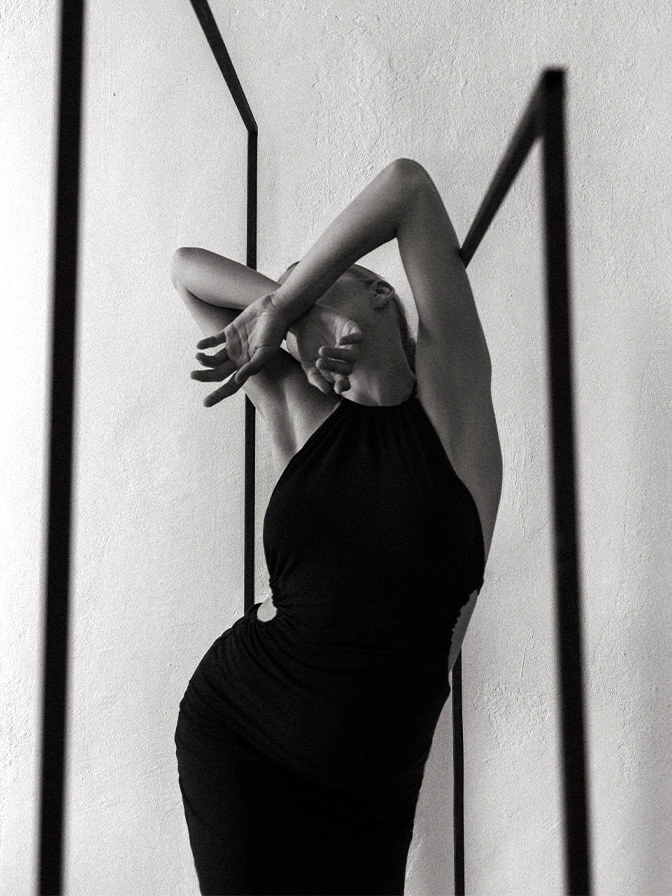 Elegant black and white portrait of woman in fitted black dress posing with raised arms against geometric striped background - arm lift in New York, NY