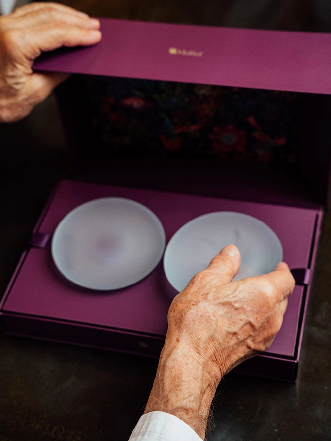 Hands opening purple gift box containing two white ceramic plates with elegant presentation - breast augmentation in New York, NY