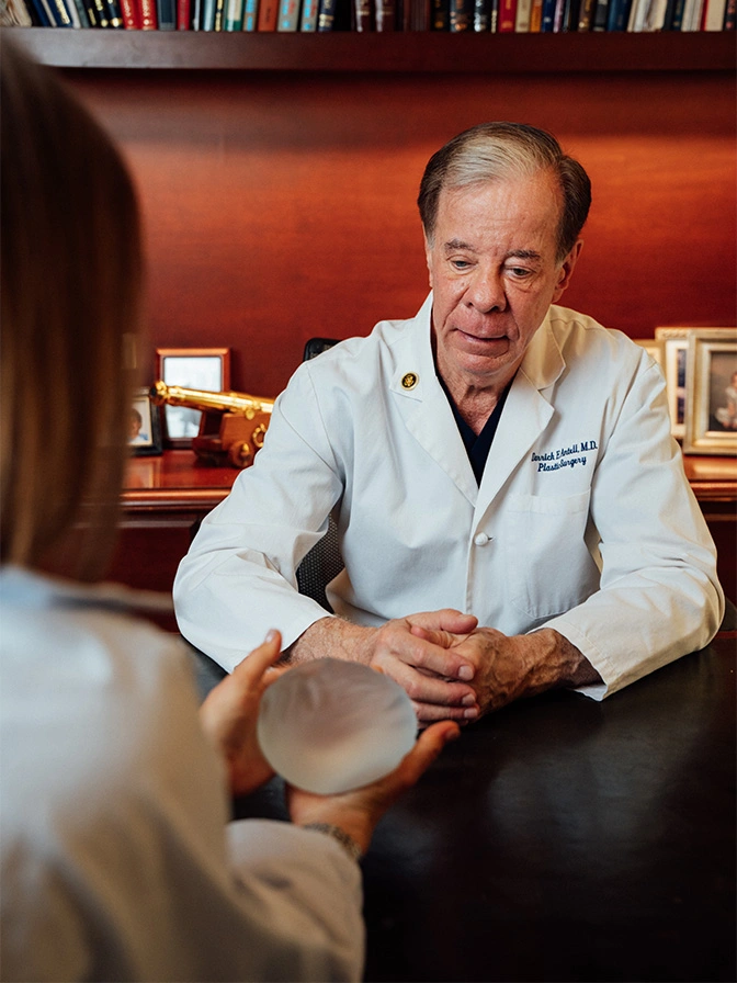 Doctor Antell in white coat consulting with patients in medical office with bookshelf background - Breast augmentation in New York, NY