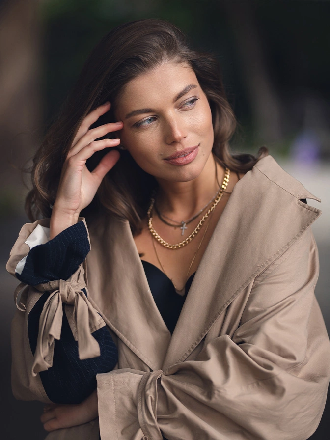 Elegant woman in beige blazer and gold necklace posing with hand near face in sophisticated portrait - brow lift in New York, NY