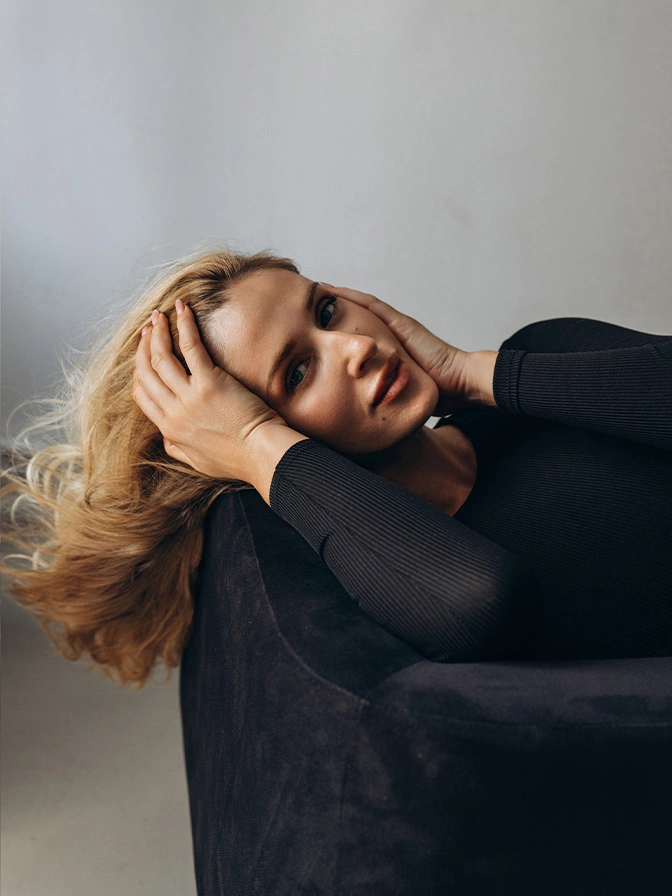 Blonde woman in black turtleneck reclining with hand in hair against white backdrop in contemplative pose - Chemical peels in New York, NY