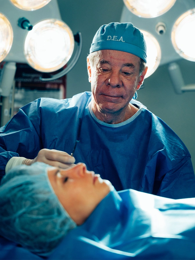 Dr Antell in blue scrubs and surgical cap performing operation in operating room with bright lights overhead - deep plane facelift in New York, NY