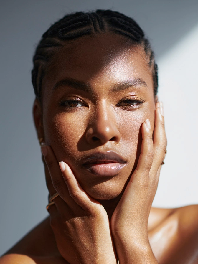 Black woman with glowing skin and natural makeup posing with hands on face in beauty portrait - dermabrasion in New York, NY