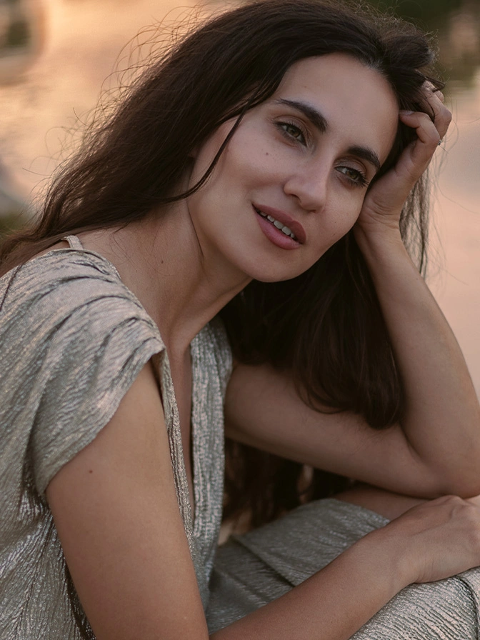 Woman with long dark hair posing outdoors in natural light wearing a light-colored dress - eyelid surgery in New York, NY