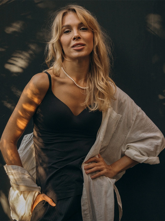 Blonde woman in black dress with white cardigan posing outdoors with natural lighting and bokeh background - facial fat transfer in New York, NY