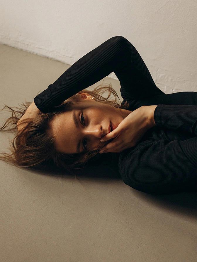 Young woman with red hair lying down in black outfit against neutral background in contemplative pose - microneedling in New York, NY