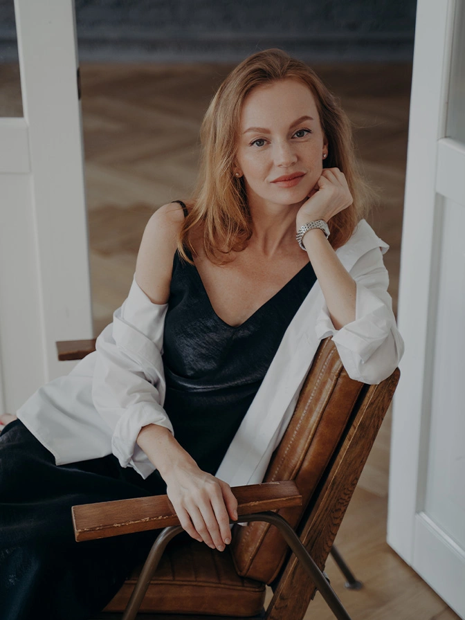 Woman in black dress and white cardigan sitting in wooden chair, elegant portrait pose - neck lift in New York, NY