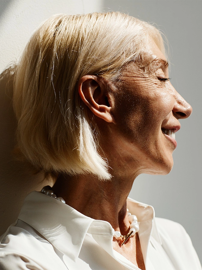Senior woman wearing hearing aid in profile view, smiling with short blonde hair and glasses - neurofibroma removal in New York, NY