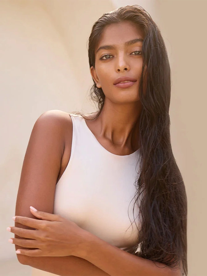 Woman with long dark hair wearing white tank top in natural lighting portrait - Nipple reduction in New York, NY