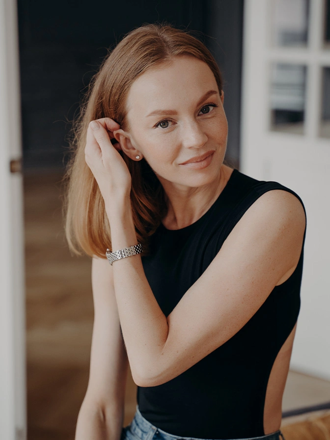 Young blonde woman in black sleeveless top posing with hand near face in bright interior setting - scar revision in New York, NY