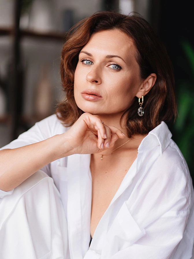 Elegant woman in white shirt with auburn hair posing thoughtfully in bright indoor setting - skin cancer in New York, NY