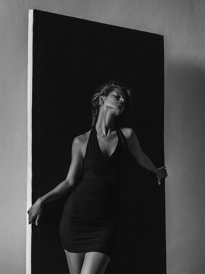 Woman in black dress standing in doorway with dramatic lighting and shadow contrast - tuberous breast correction in New York, NY