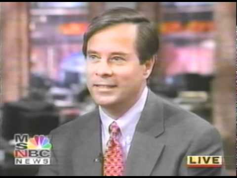 News anchor in suit and tie reporting live from television studio broadcast desk
