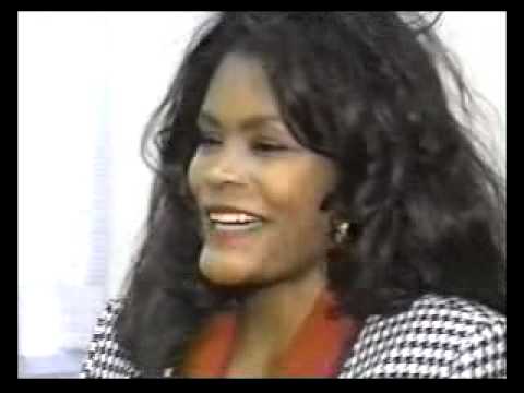 Woman with long dark hair smiling in houndstooth jacket during press interview or media appearance