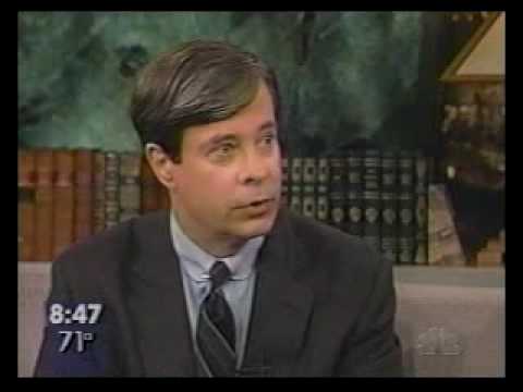 Man in suit and tie during television interview with time stamp 8:47 and temperature 71° displayed on screen