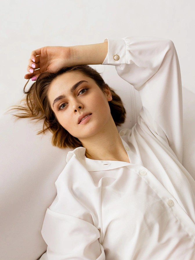 Woman in white oversized shirt with short brown hair posing with arm raised against neutral background - latiesse in New York, NY